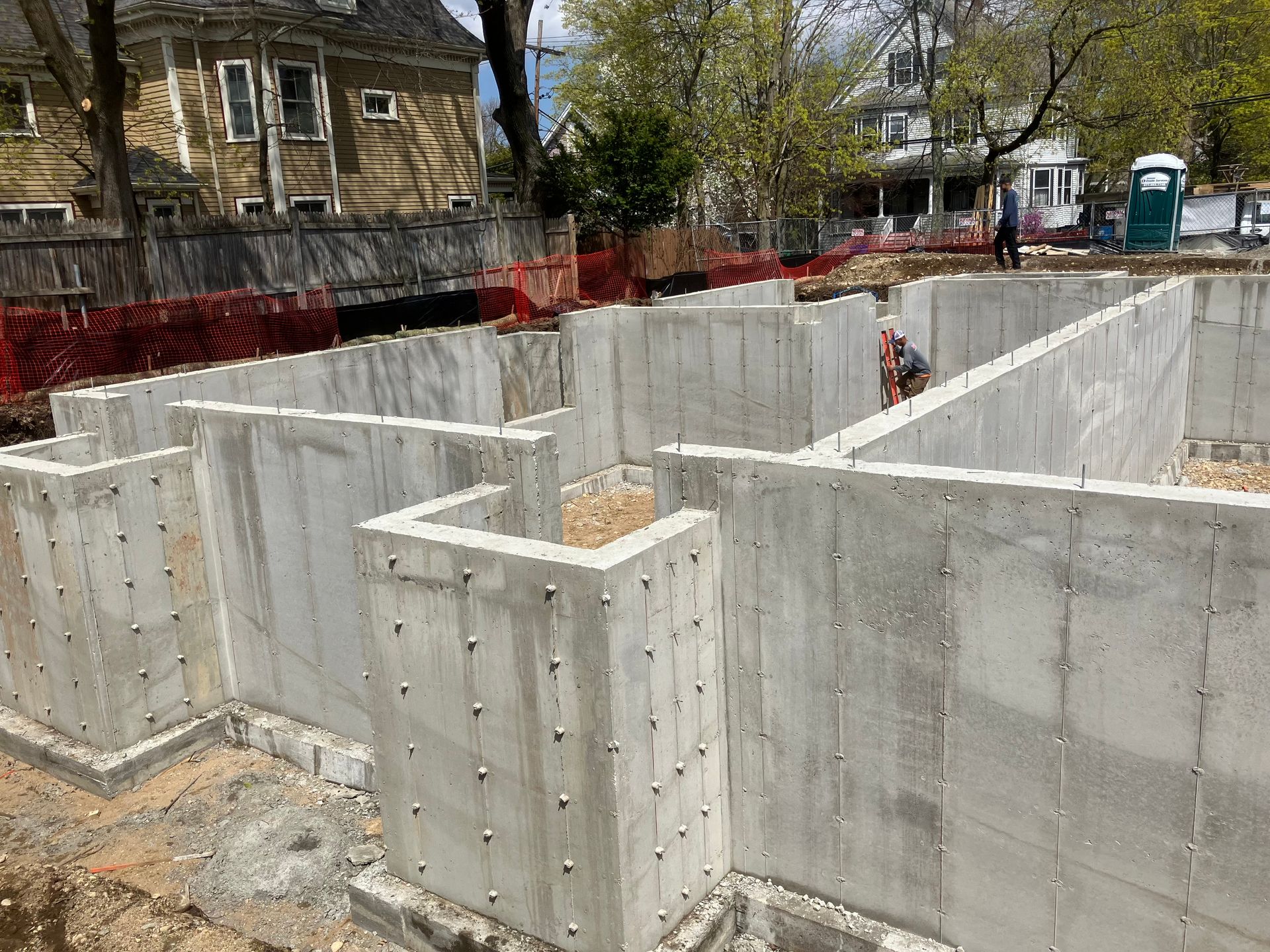 Concrete foundation walls under construction at a building site with a portable toilet and fencing.
