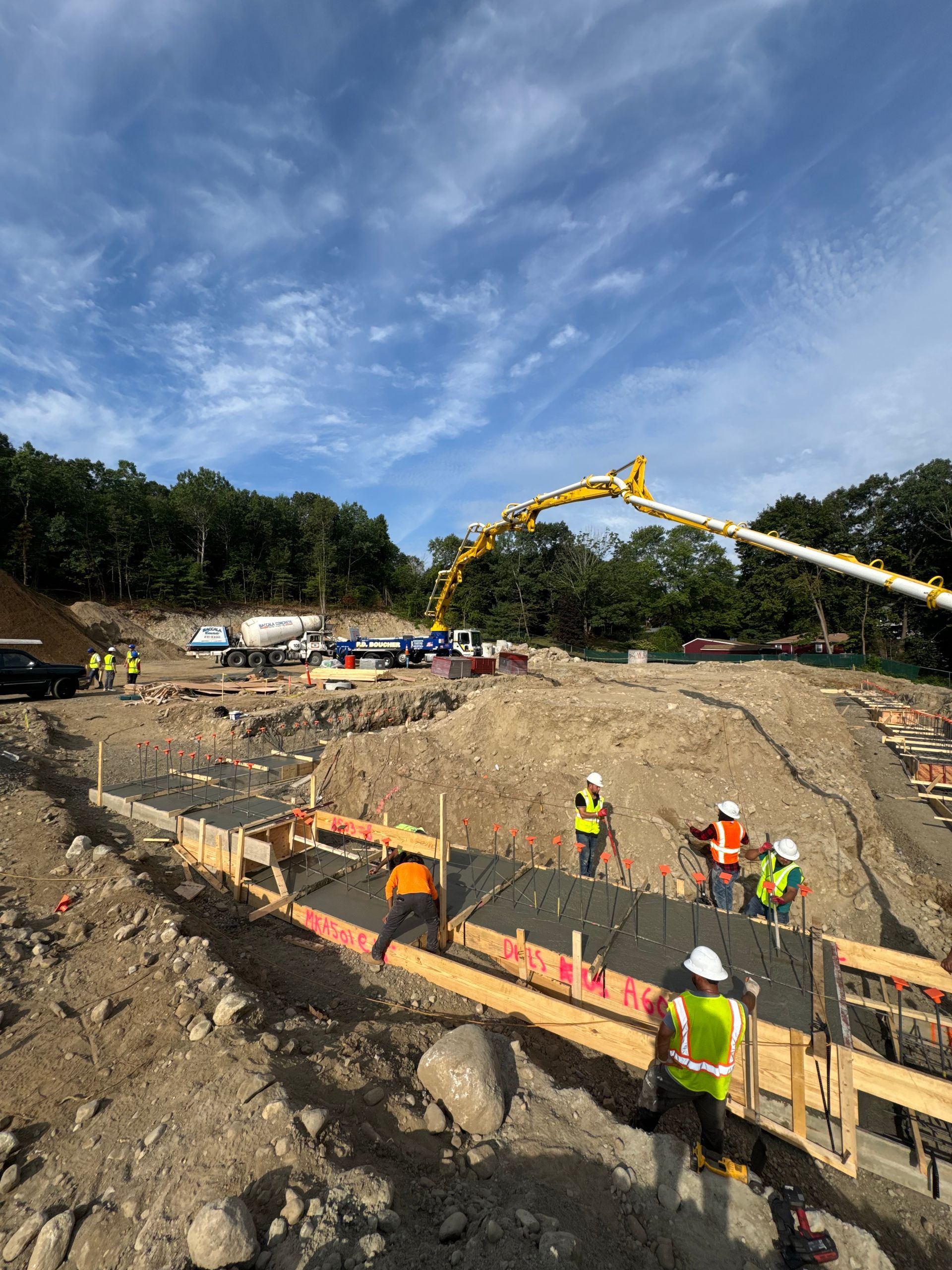 Construction site with workers pouring concrete. A pump truck is pouring concrete into a wooden frame.