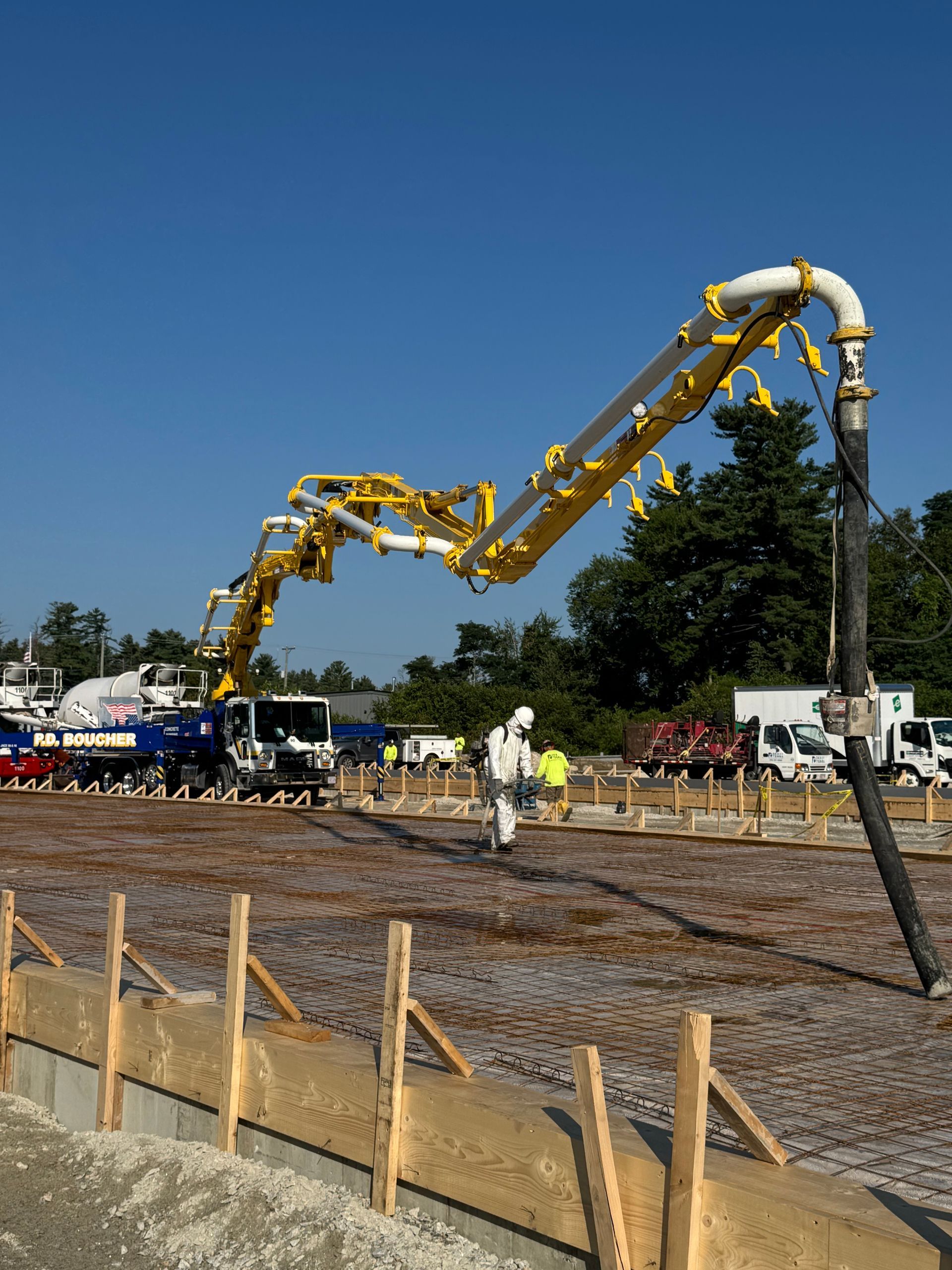 Concrete pump pouring concrete on a construction site; yellow arm, blue sky.