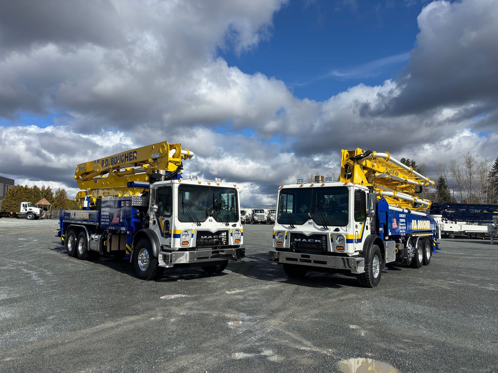 Two concrete pump trucks parked on gravel under a cloudy sky.