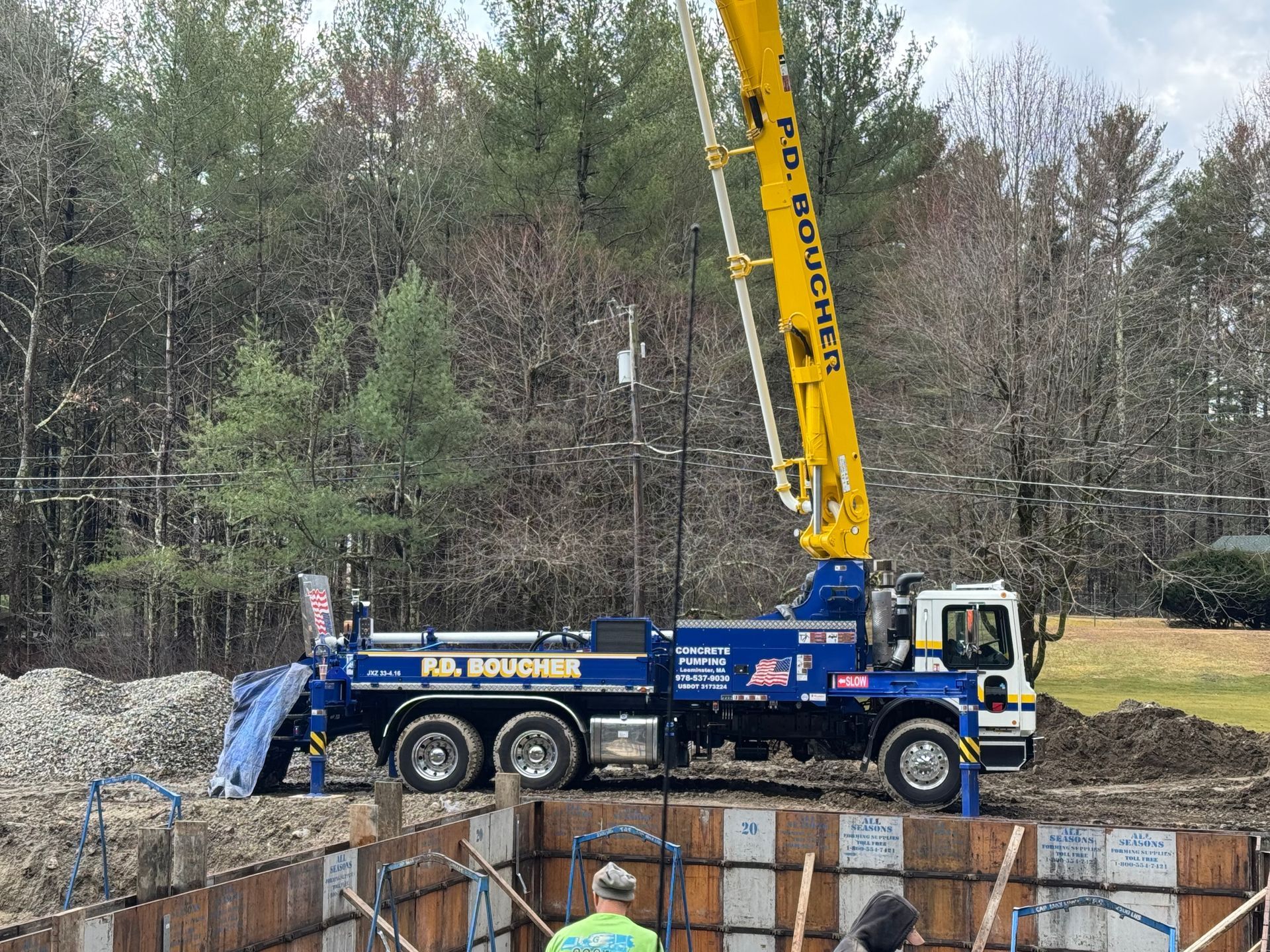 Concrete pump truck pouring concrete into a form. Yellow boom, blue truck, construction site.