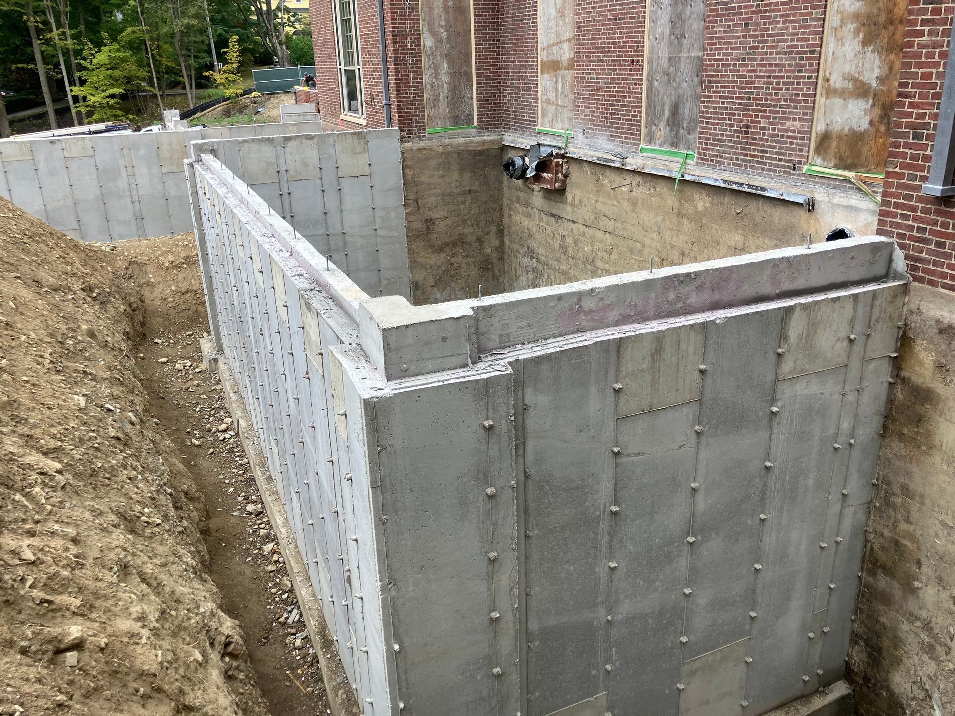 Concrete retaining walls, forming a recessed area near a brick building under construction; dirt and excavation visible.