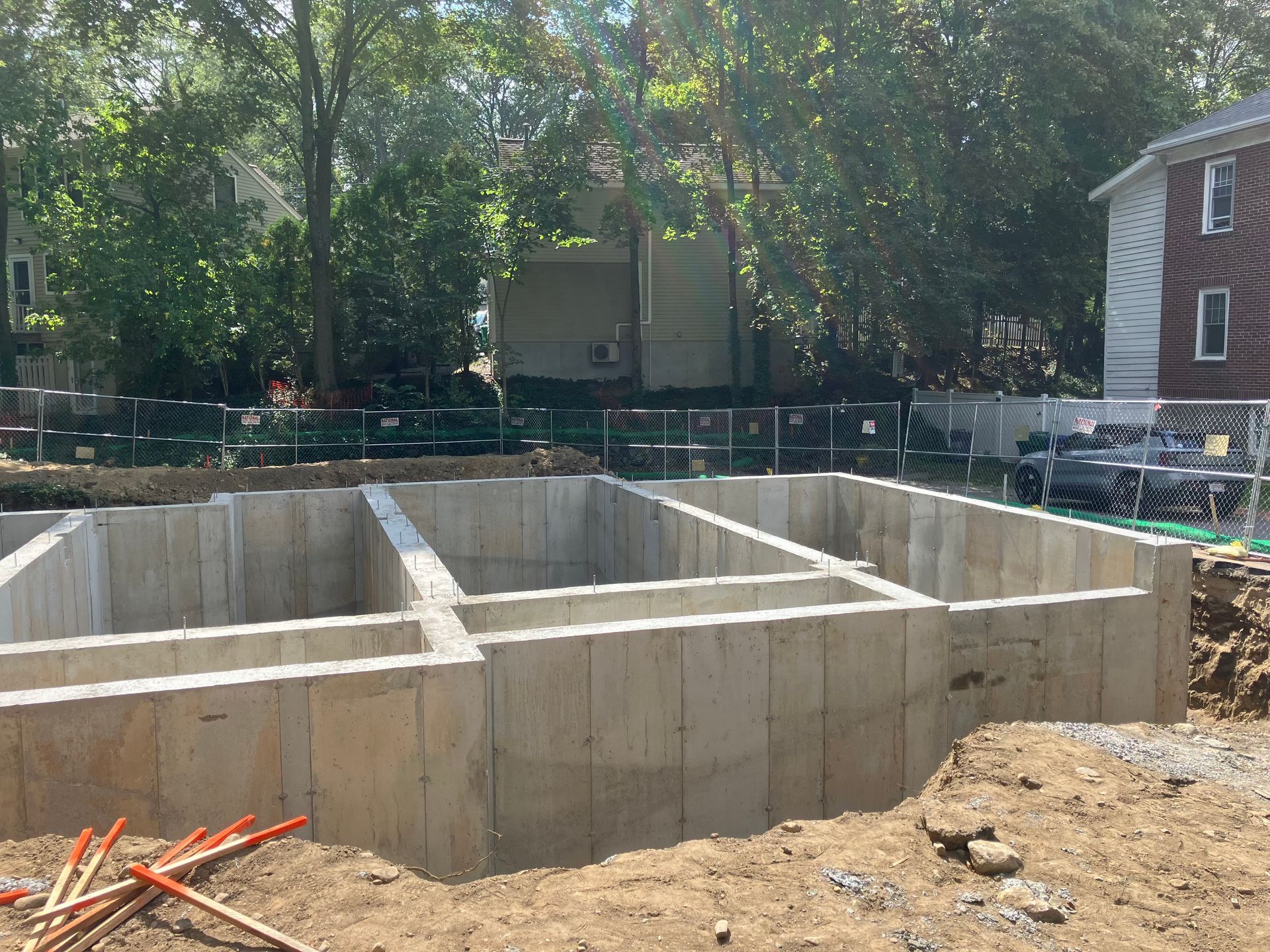 Concrete foundation walls of a building under construction, with dirt, trees, and fencing in the background.