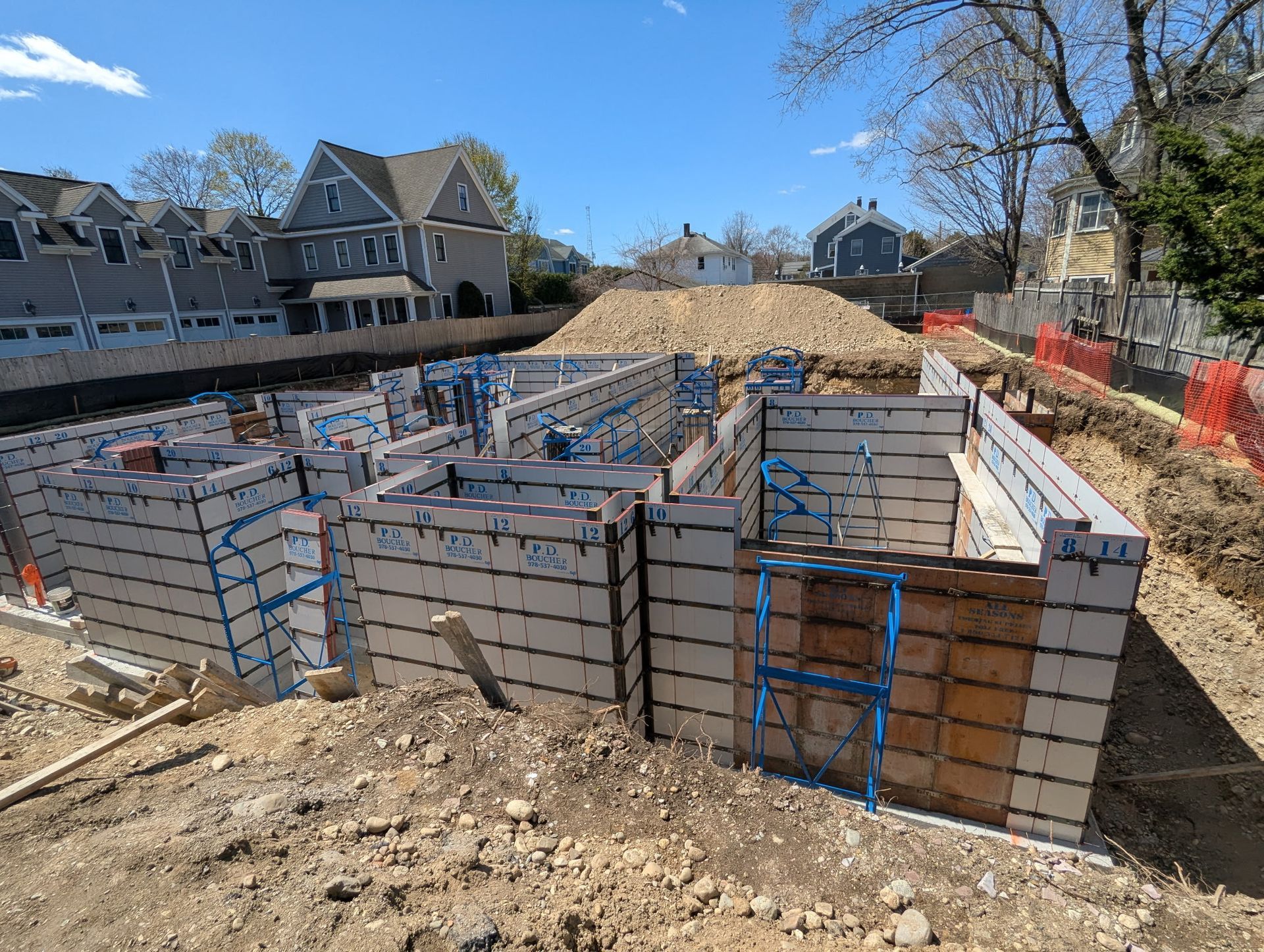 Construction site with concrete forms for a building foundation, surrounded by earth and orange safety fencing.
