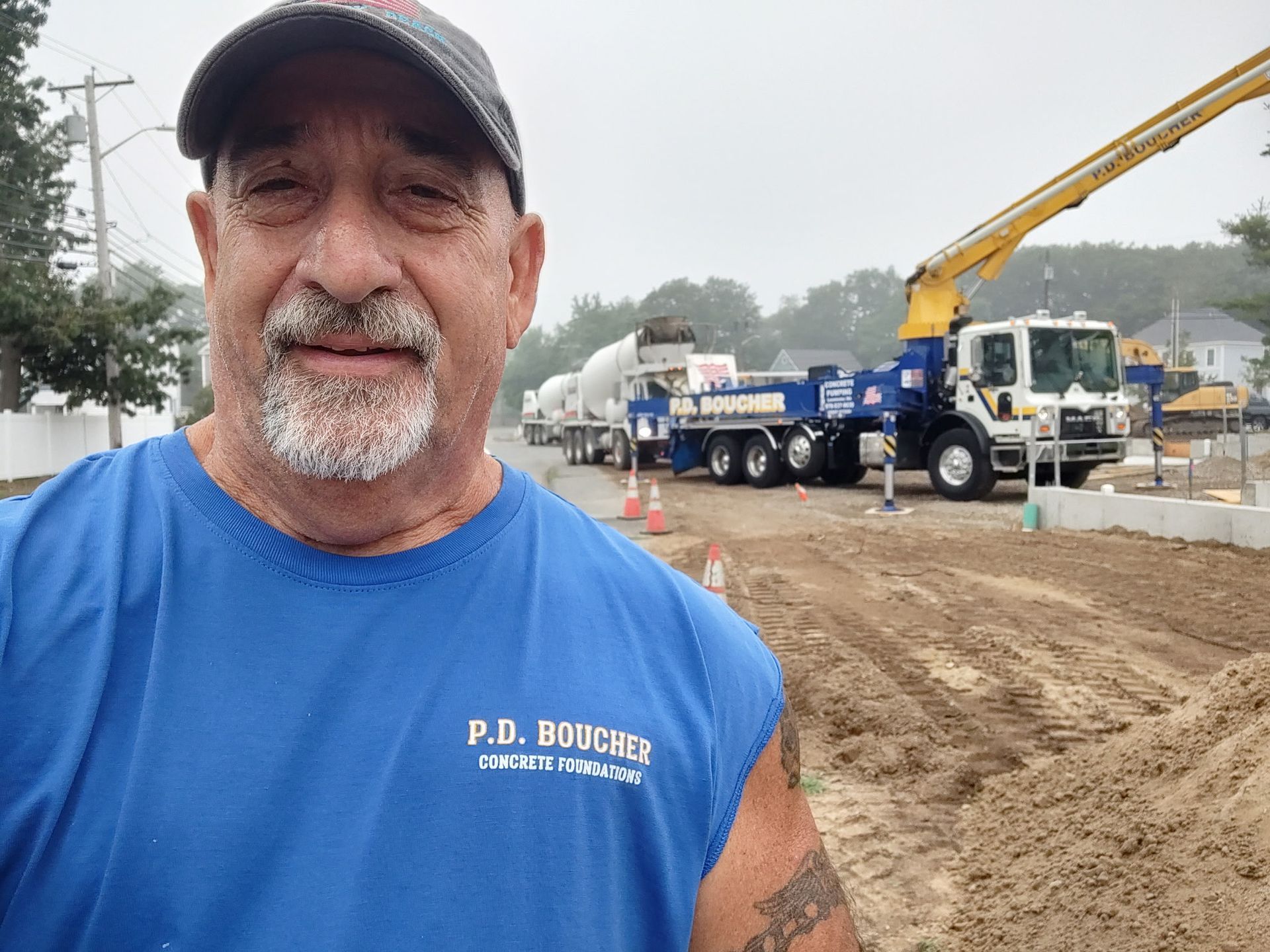 Man in blue shirt, construction site with concrete pump truck. Cloudy day.