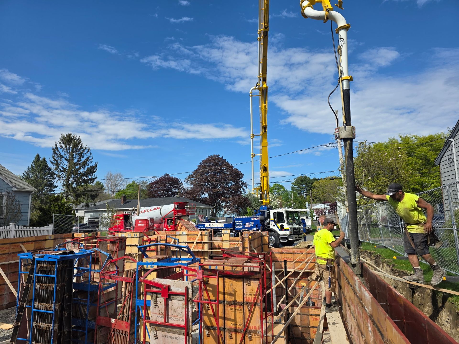 Construction site with workers, concrete forms, and pump truck under a blue sky.