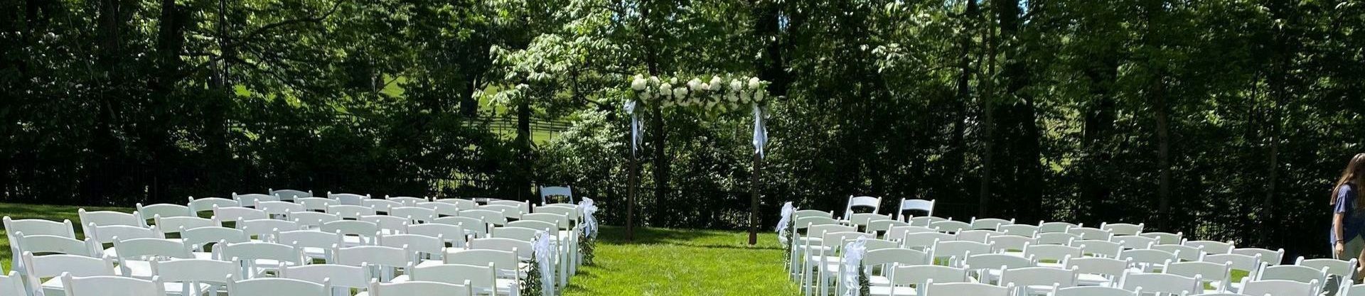 a row of white chairs are lined up in a grassy field .