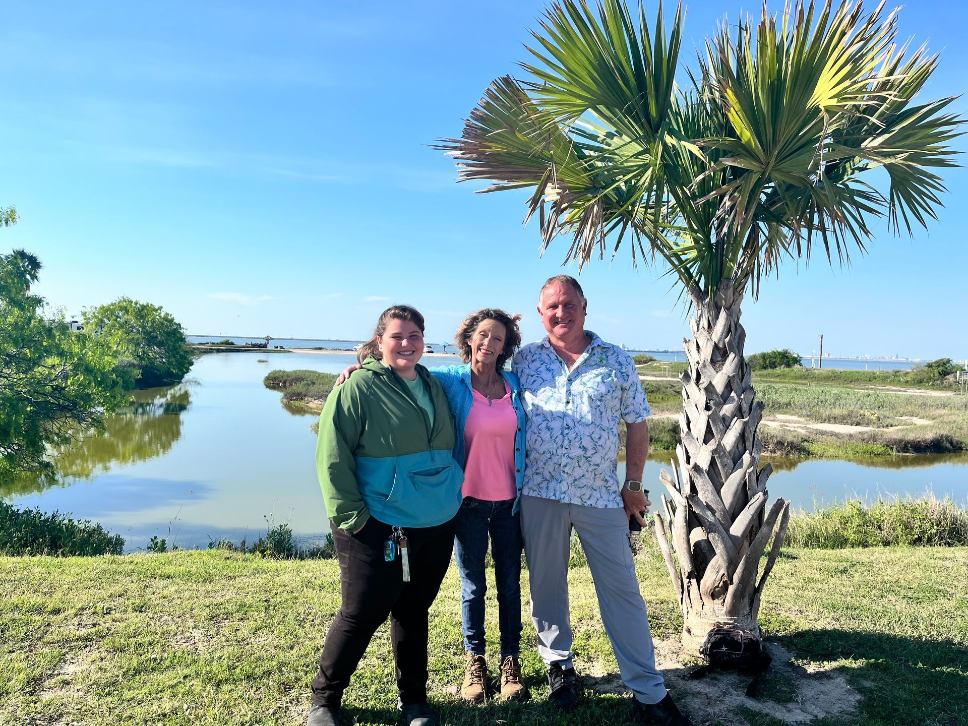 Three people are posing for a picture in front of a palm tree.