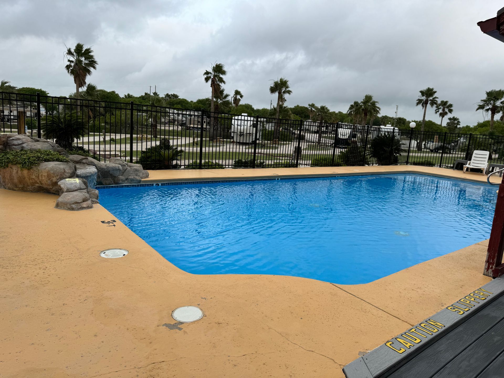A large swimming pool with a fence around it and palm trees in the background