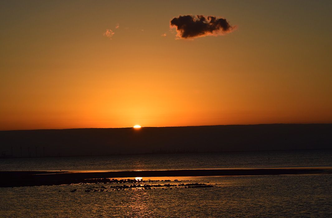 The sun is setting over the ocean with a cloud in the sky.