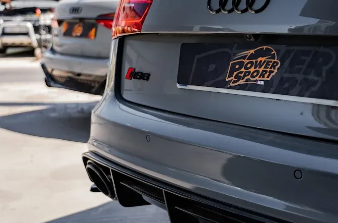 Vista de cerca de la parte trasera de un Audi RS3 gris, donde se aprecian su emblema negro, el marco de la matrícula y el difusor deportivo.