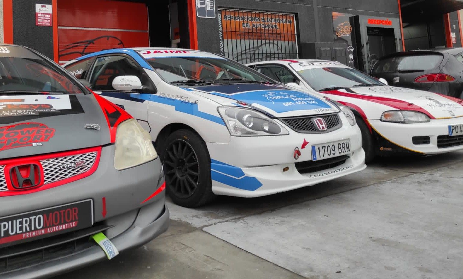 Tres coches Honda modificados, con calcomanías de carreras y una pintura deportiva, estaban aparcados frente a un garaje.