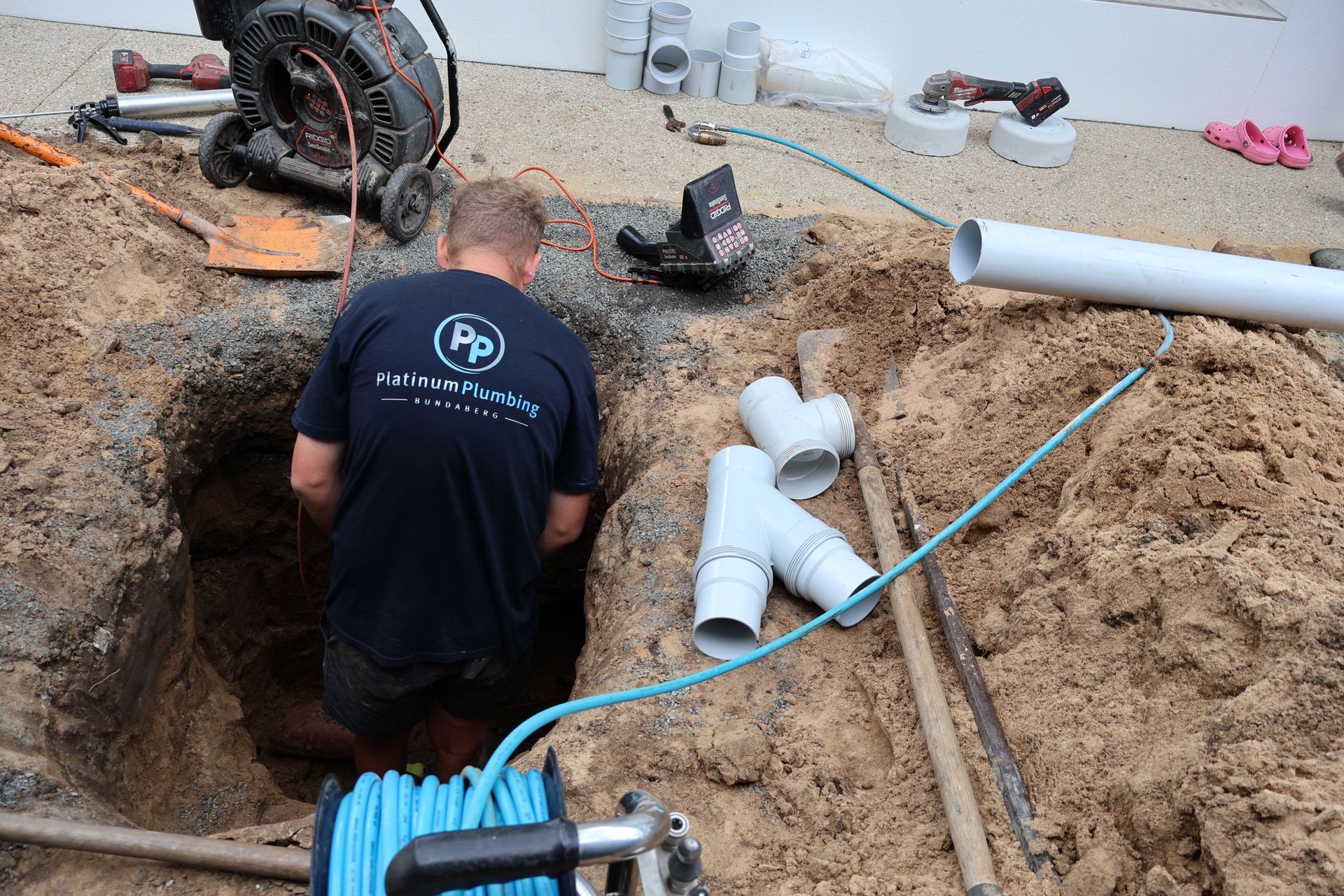 Worker installing white PVC pipes in a sandy trench at a construction site