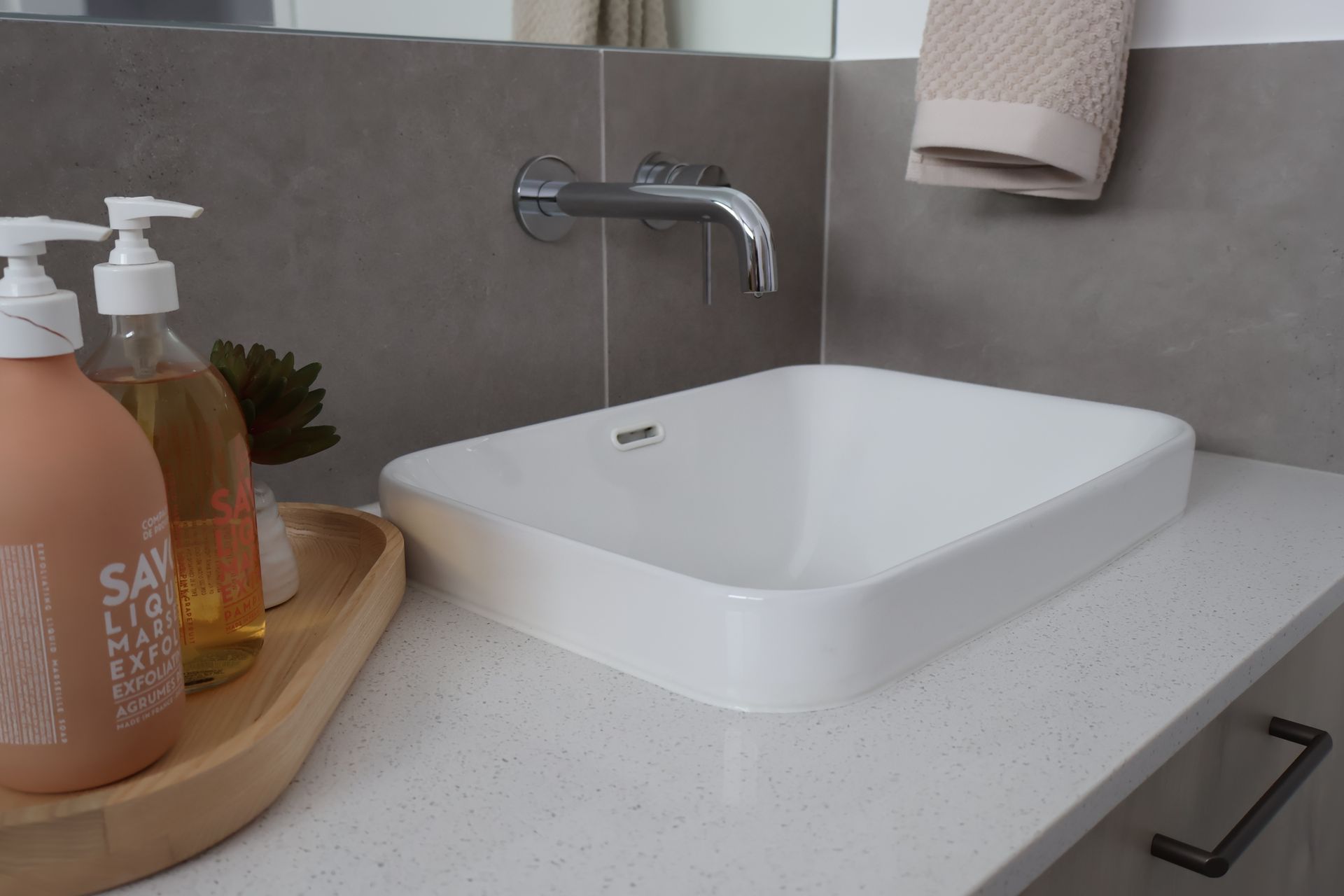 Modern bathroom sink with chrome faucet, white countertop, soap dispenser, and towel rack