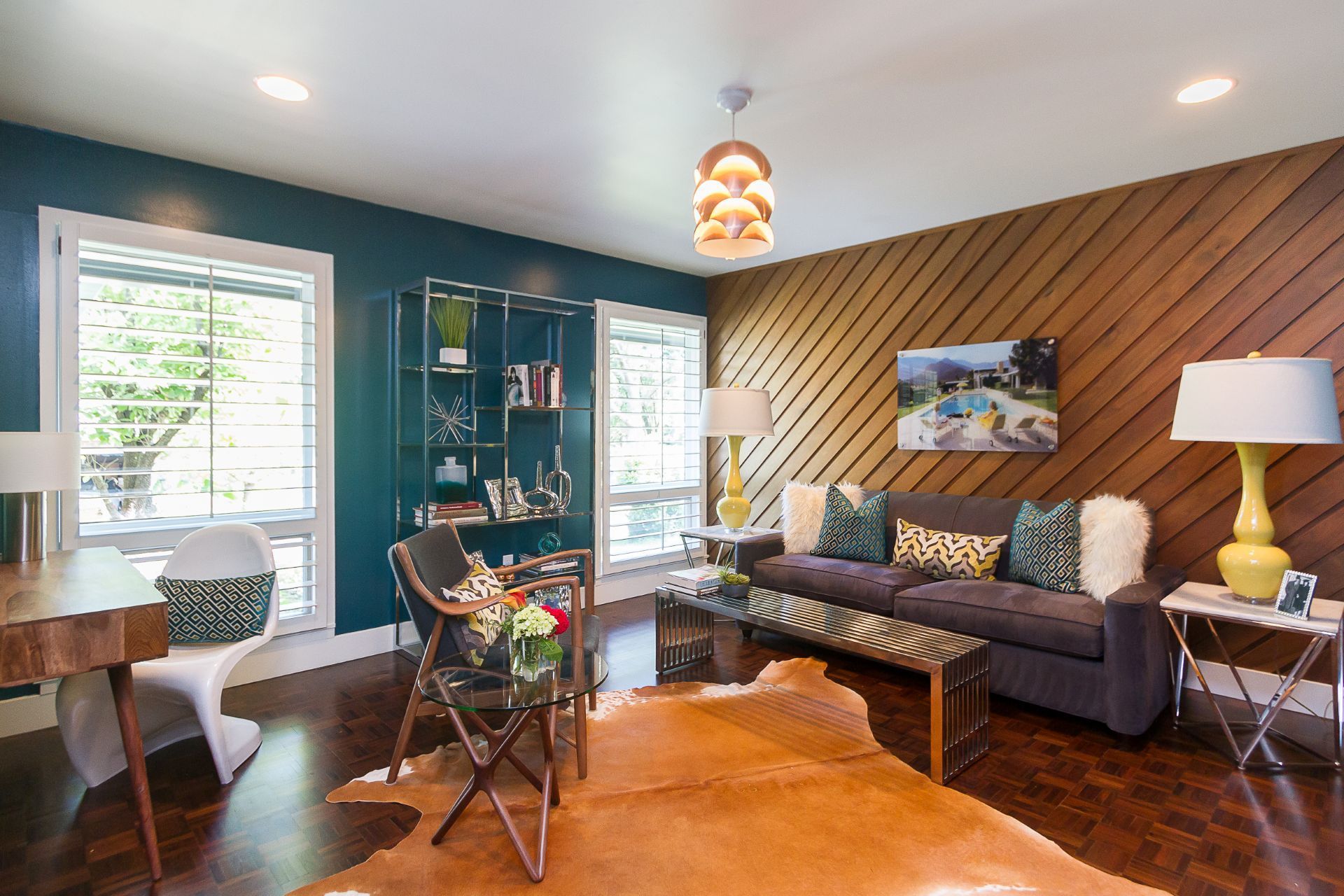 A living room with a couch , desk , chairs , lamps and a cowhide rug.