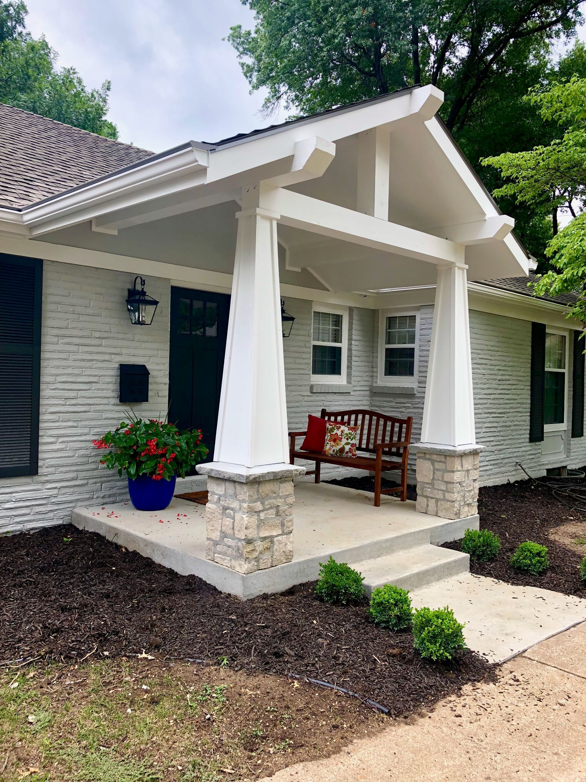 A white brick house with a porch and a bench.