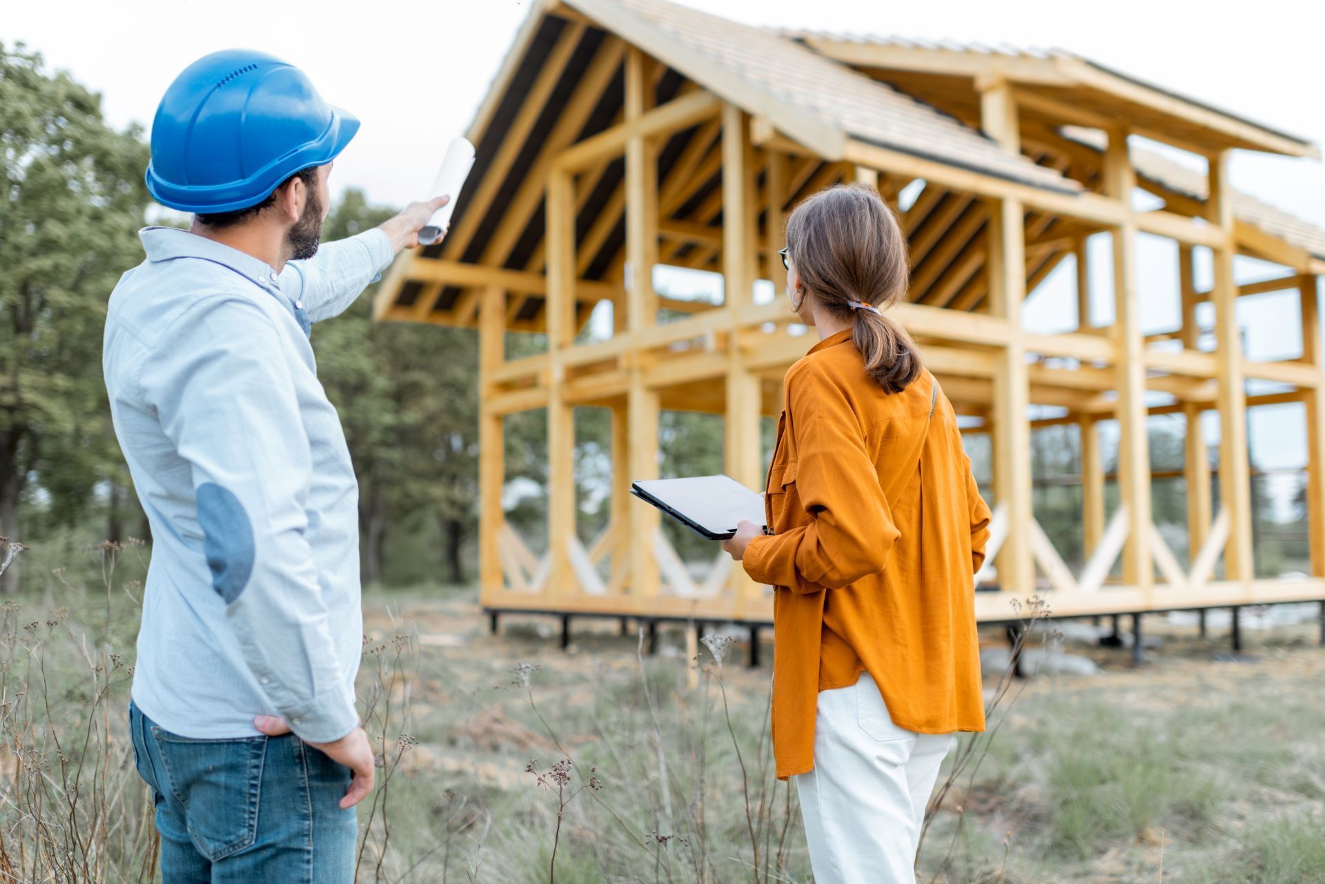 A man in a blue hard hat and woman looking at a wooden house under construction.