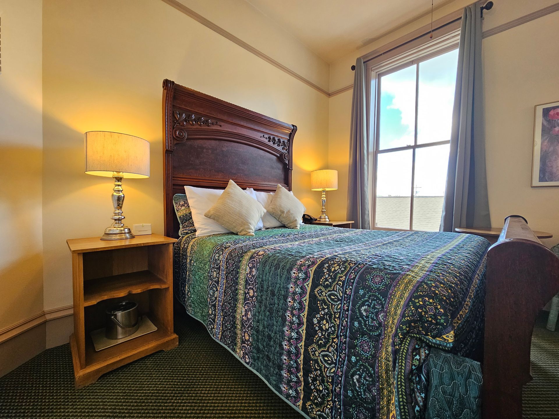 A hotel room with a bed , nightstand , lamps and a window.