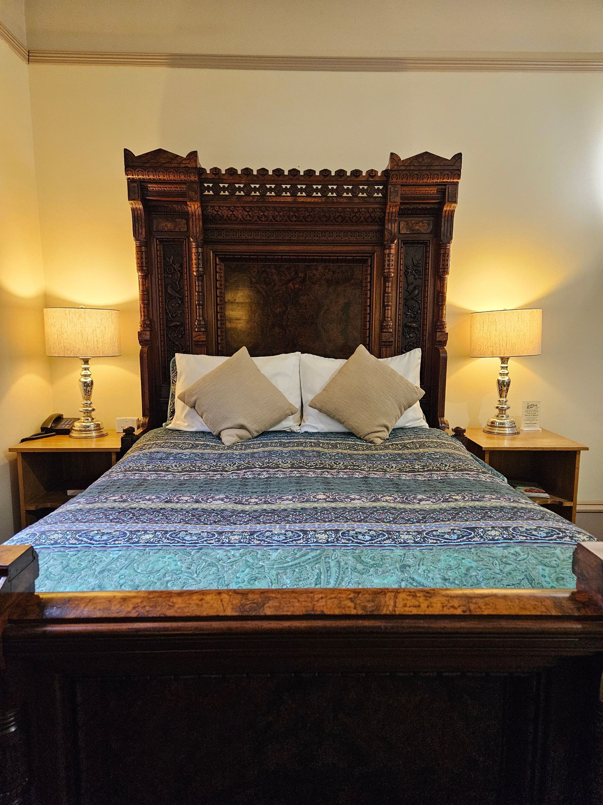 Ornate wooden headboard and bed with bedside lamps in a bedroom.
