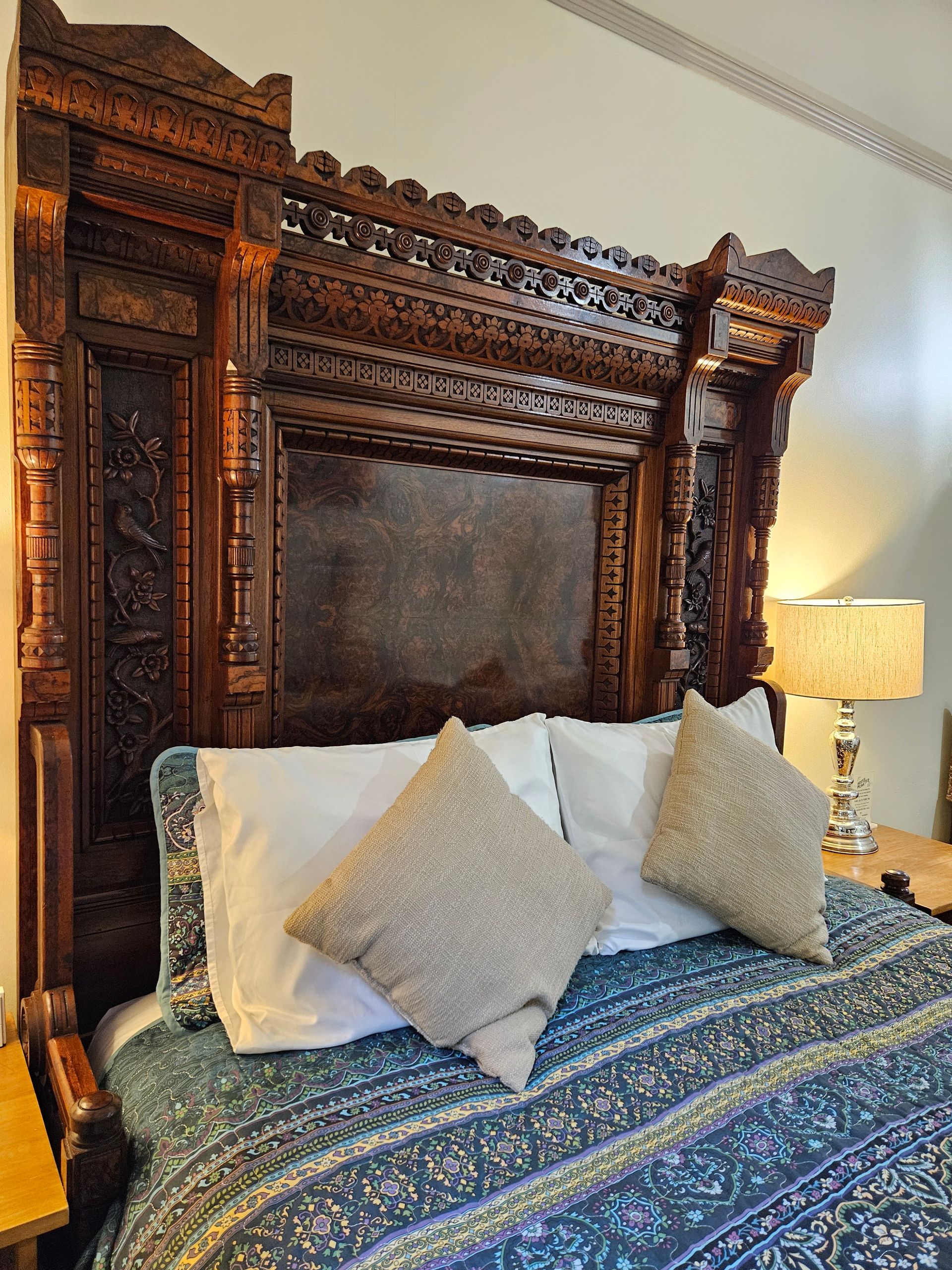 Ornate dark wood headboard above a bed with pillows and patterned comforter.