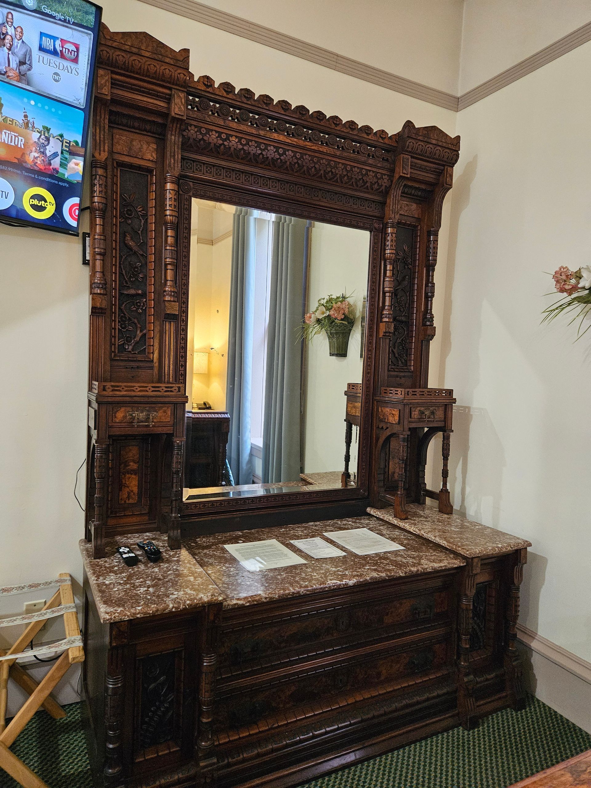 Ornate wooden dresser with large mirror, dark wood carving, marble countertop, and built-in side tables.