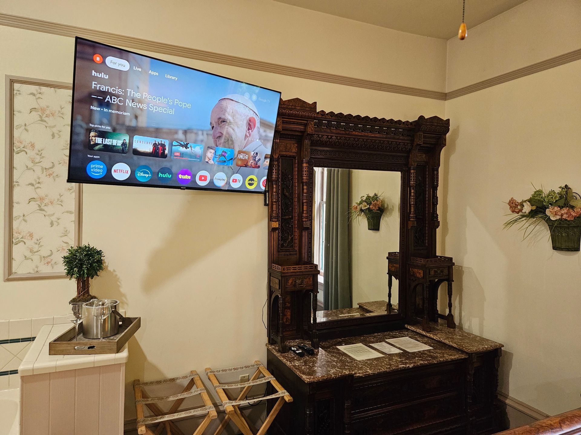 Bedroom with TV, ornate dresser, and small side table. Walls are light beige.