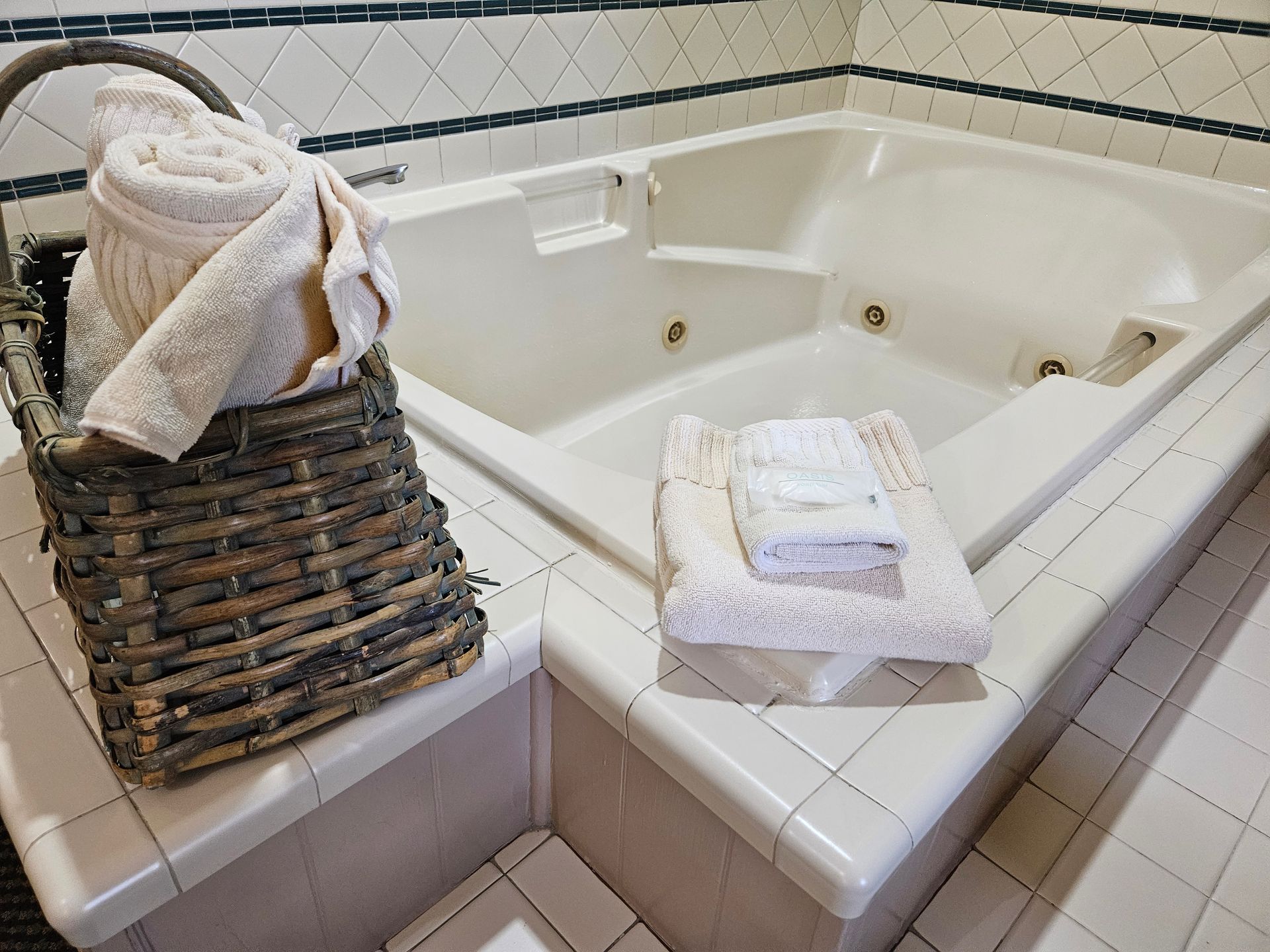 Bathroom with a white jacuzzi tub. A basket of towels is next to the tub, and a stack of towels sits on the ledge.