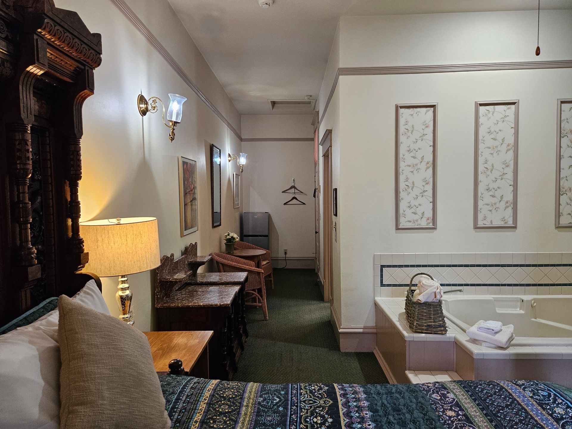 Hotel room with a large bed, desk, and jacuzzi tub. The hallway leads to a doorway.