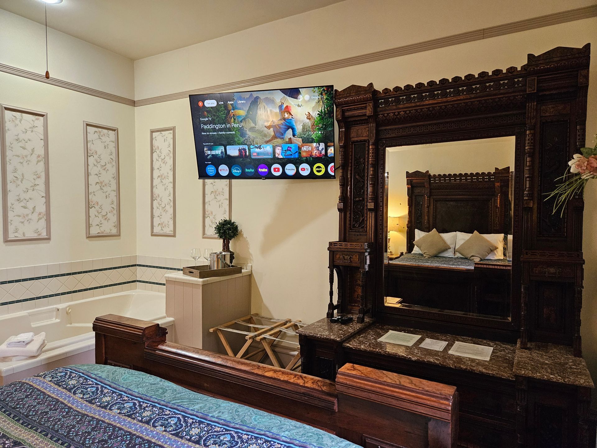 Bedroom with ornate dark wood furniture, TV on the wall, and a jacuzzi tub.