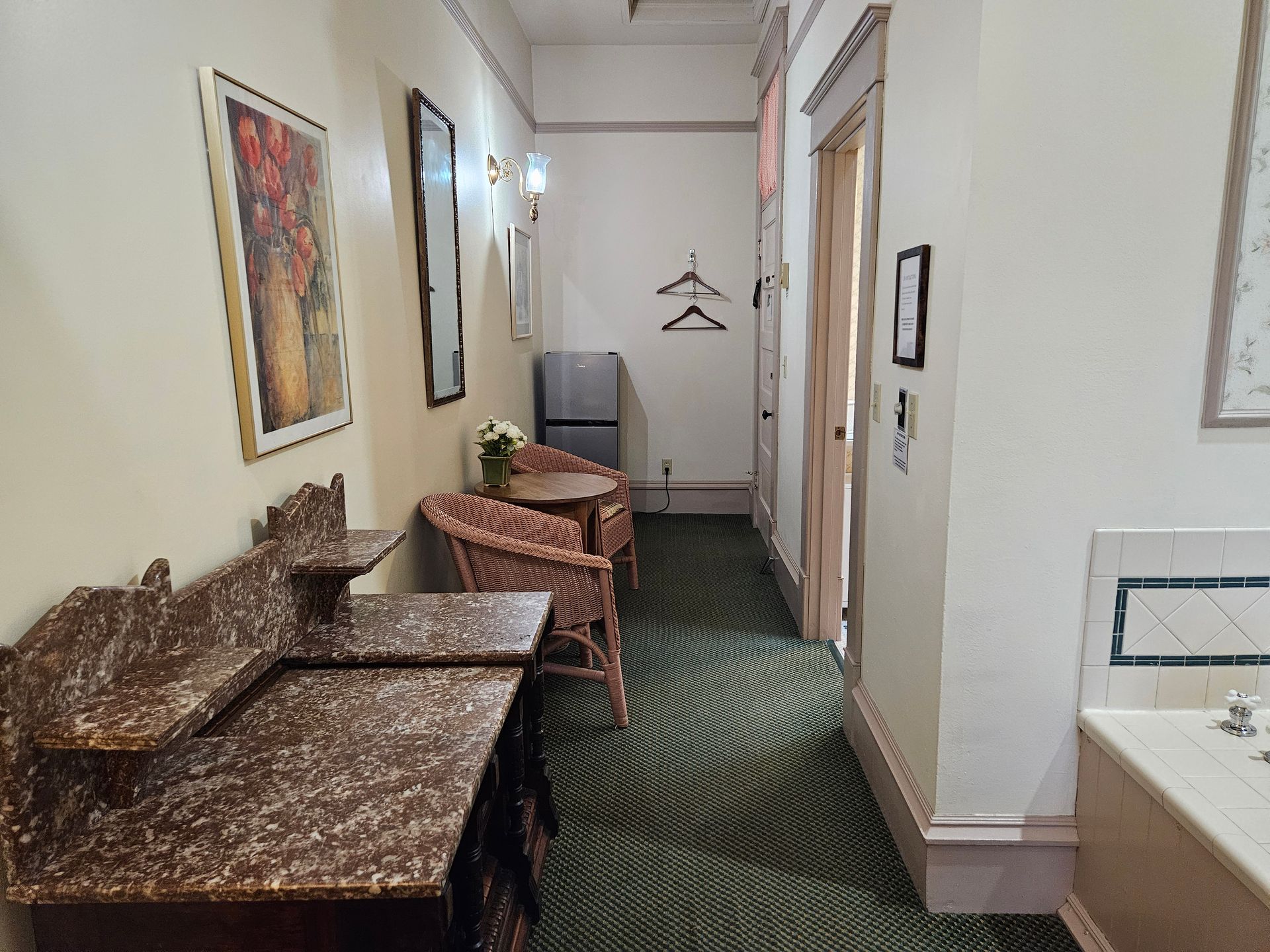 Narrow hallway with patterned carpet, ornate seating, and a door.