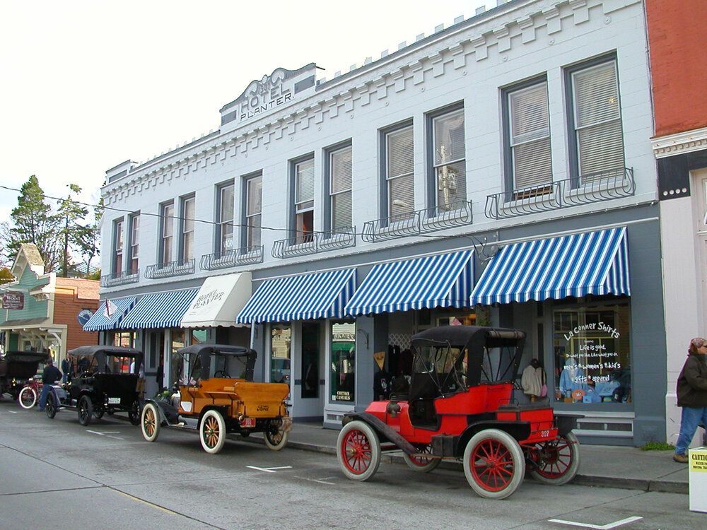 Three old cars are parked in front of a building with blue and white awnings