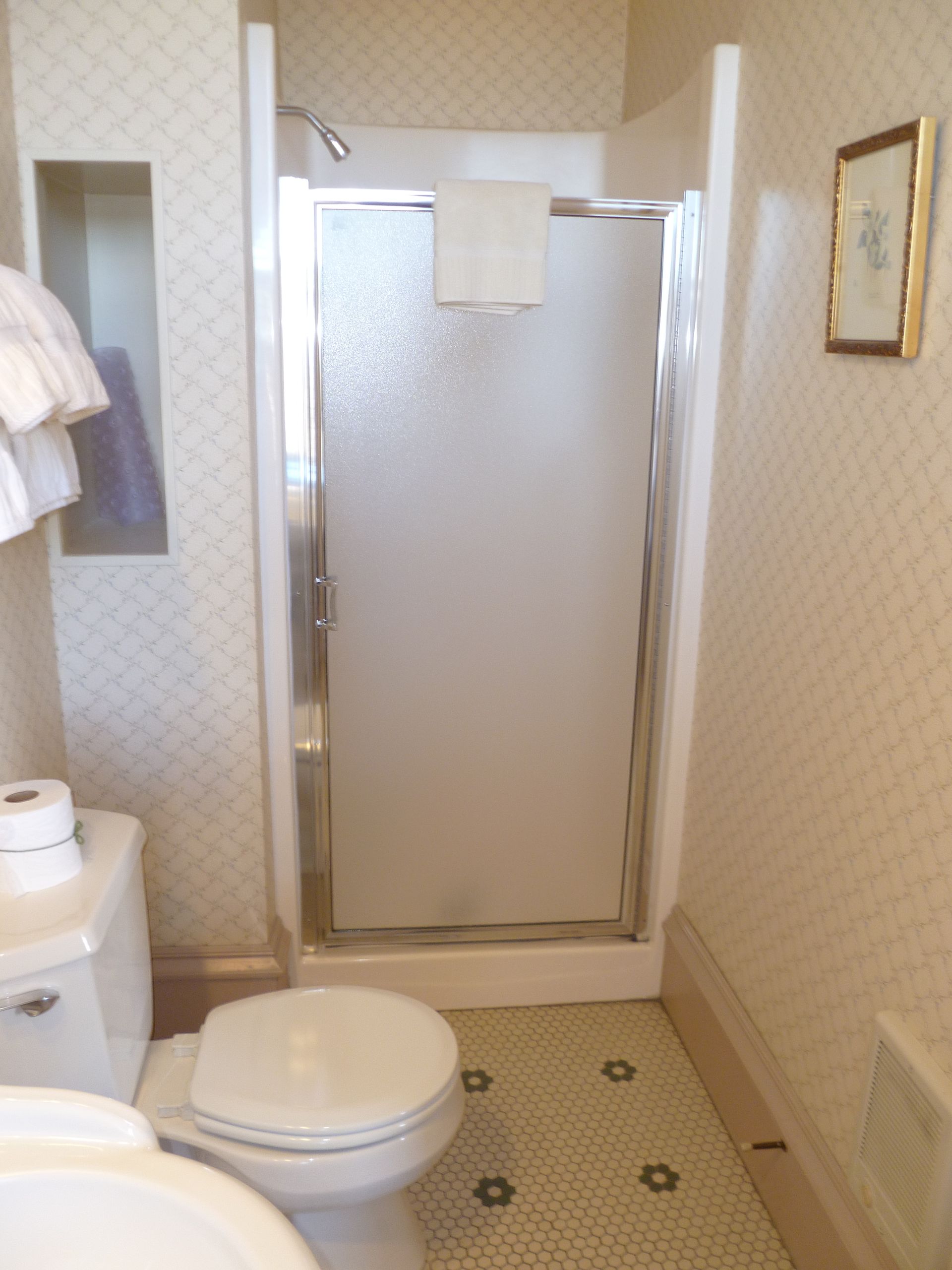 Bathroom with white toilet, shower with frosted glass door, towels, and decorative wallpaper.