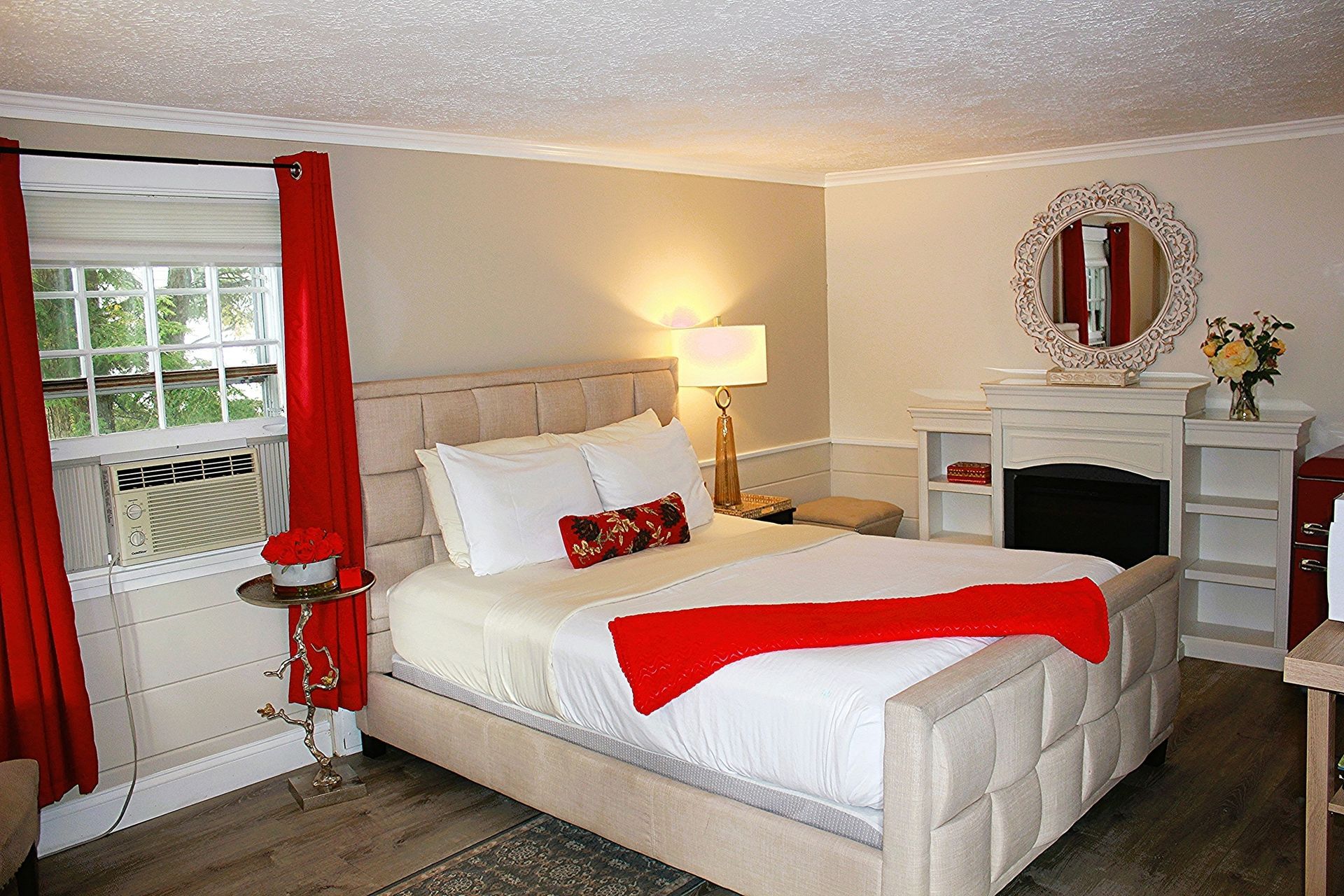 Bedroom with a bed, fireplace, window with red curtains, and decorative mirror.