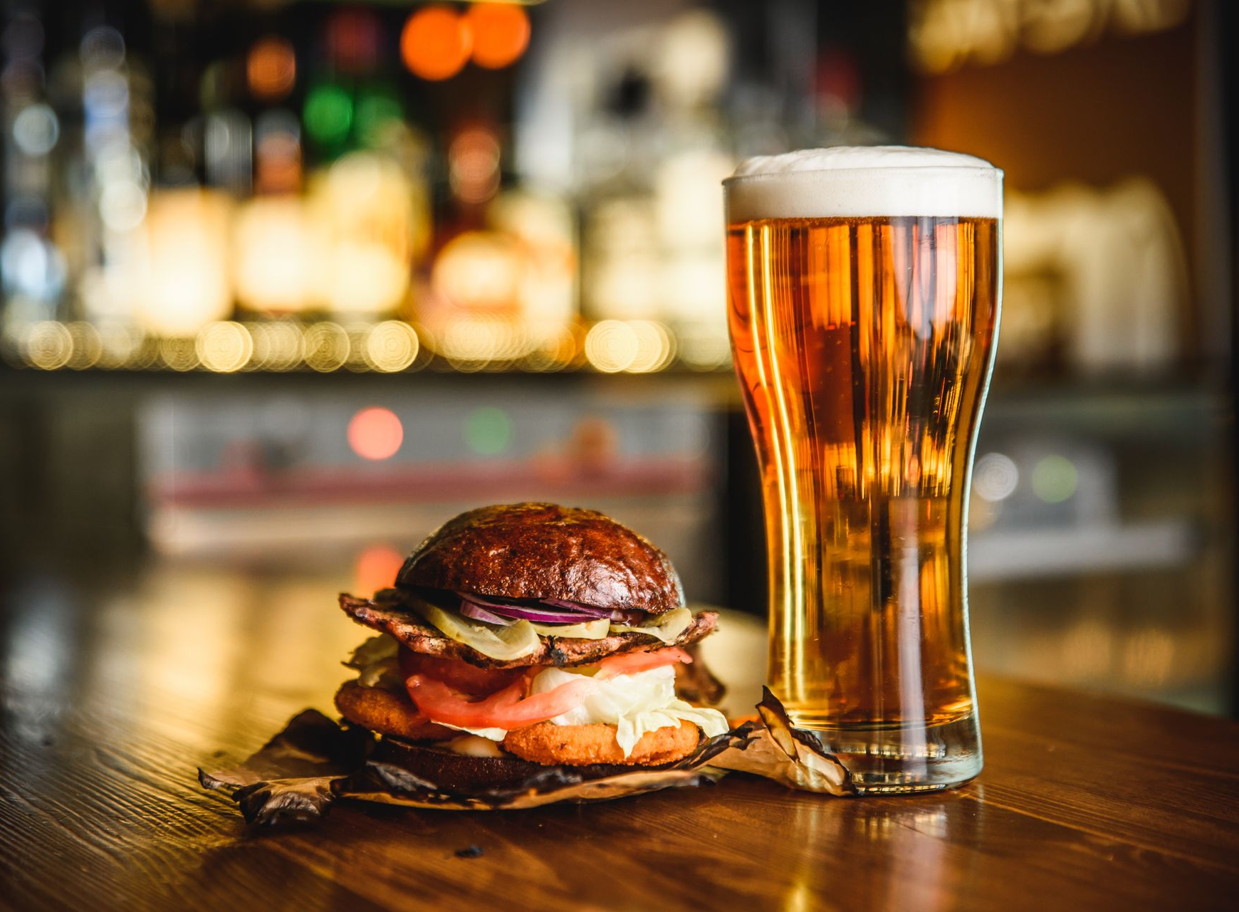 Burger on wood with beer in glass, bar background.
