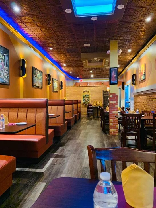 Restaurant interior with round tables set for dining, red tablecloths, black chairs, and dark red walls.