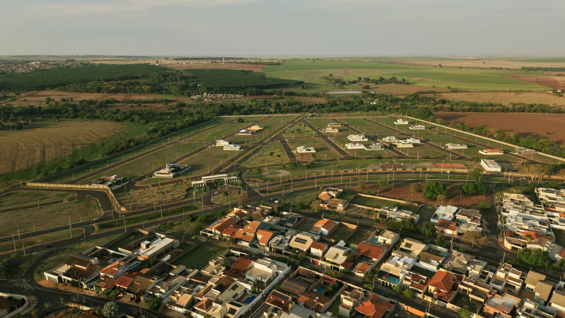 Vista aérea de um bairro residencial com casas e um loteamento triangular em um ambiente rural.