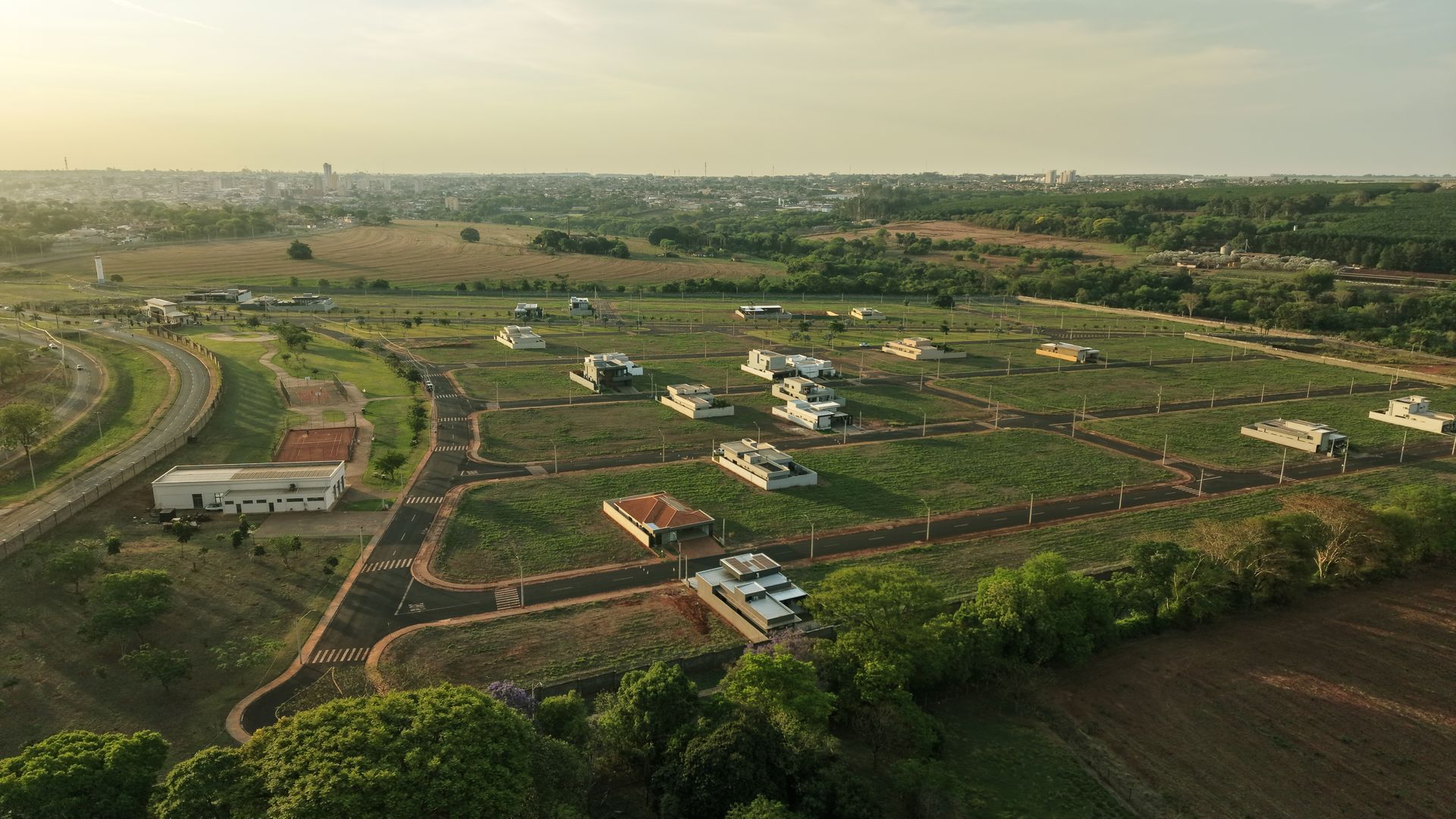 Vista aérea de um conjunto residencial com várias casas, ruas e áreas verdes sob um céu limpo.
