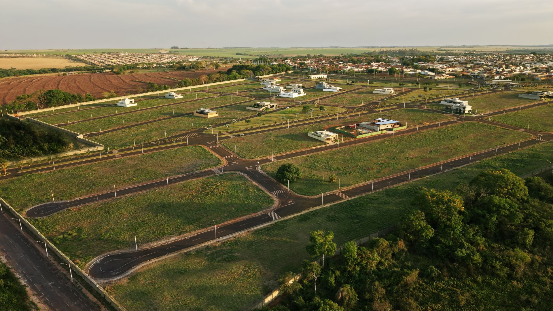Vista aérea de um loteamento suburbano com terrenos baldios e algumas casas já construídas.