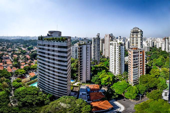 Vista da cidade com arranha-céus e árvores verdes sob um céu azul brilhante.