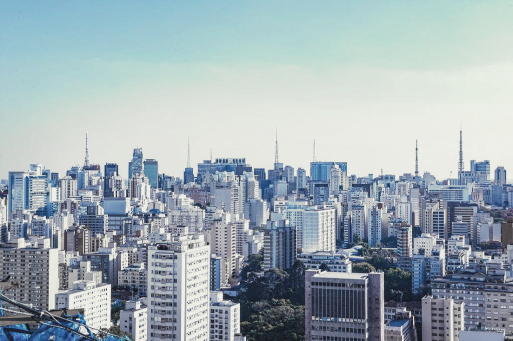Vista da cidade com inúmeros arranha-céus sob um céu claro e azul-claro.