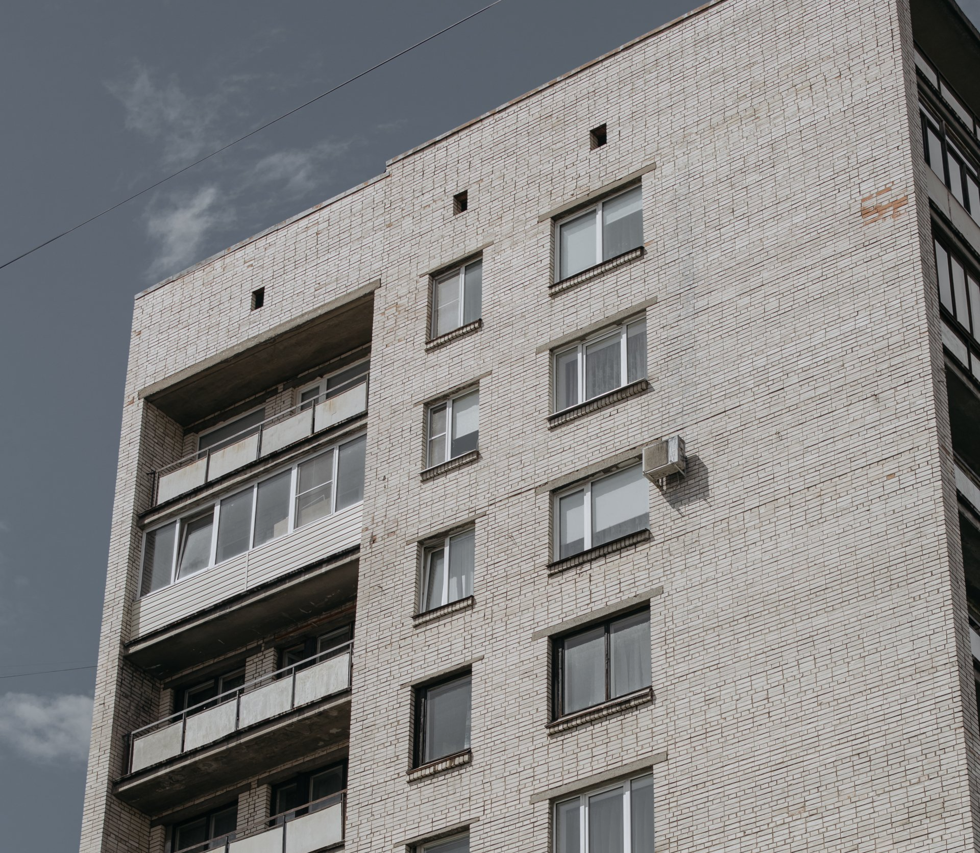 Prédio de apartamentos de tijolos cinza contra um céu nublado; varandas e janelas visíveis.
