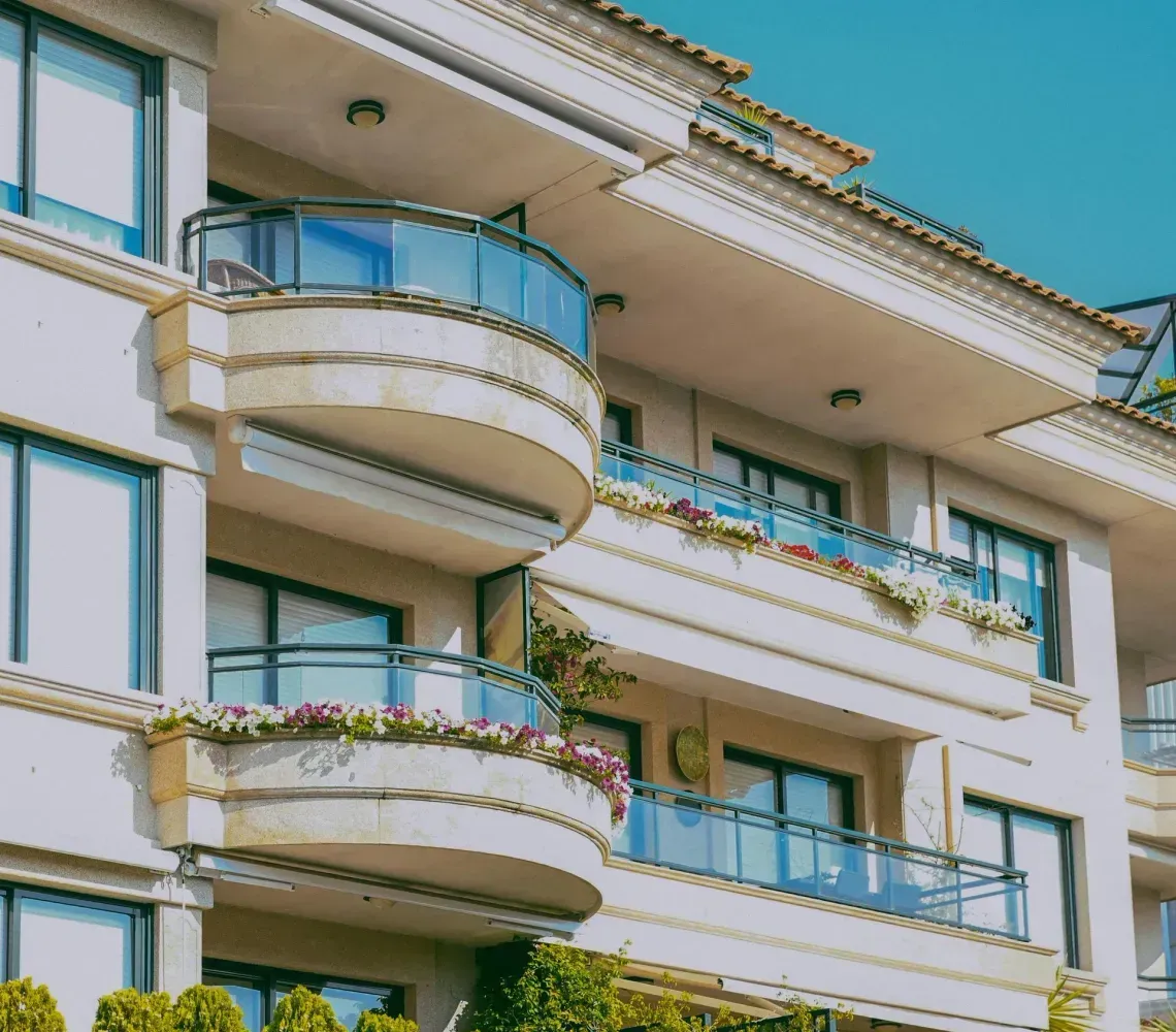 Modern apartment balconies with blue glass railings and flower boxes under a sunny sky