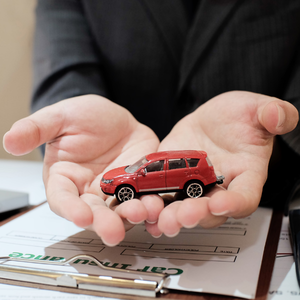 Hands holding a small red toy SUV above paperwork on a desk
