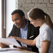 Two colleagues reviewing a document together at a desk, smiling in a bright office.