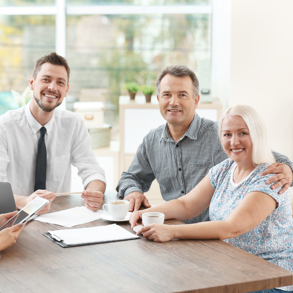 Three people smiling around a conference table with papers in a bright office