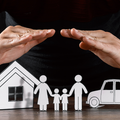 Hands shielding paper house, family, and car icons on black background
