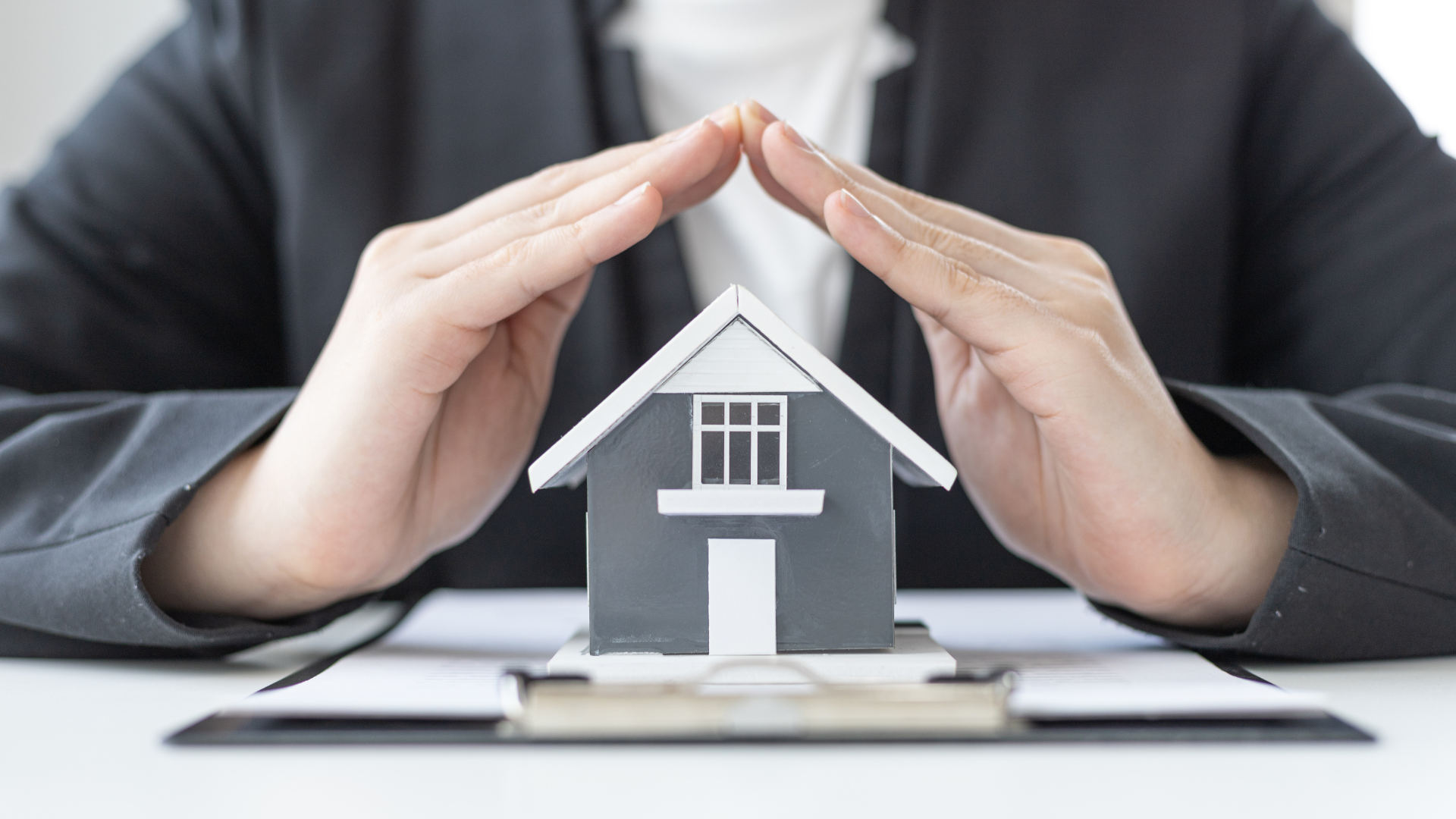 Hands sheltering a small house model on stacked books, symbolizing home protection or insurance