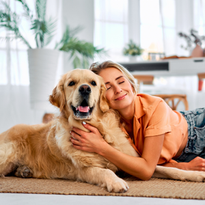 Woman cuddling a golden retriever on a living room floor, both relaxed and smiling