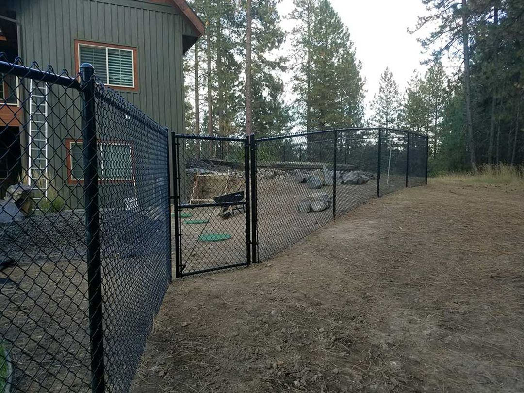 A chain link fence surrounds a house in the woods