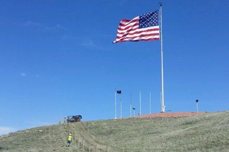 A large american flag is flying over a grassy hill